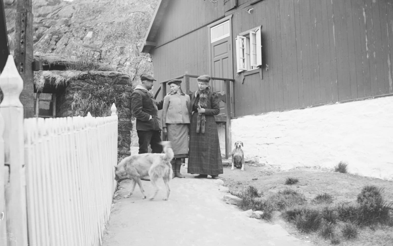 En man och två kvinnor står och samtalar framför ett trähus på Grönland, med en hund i förgrunden