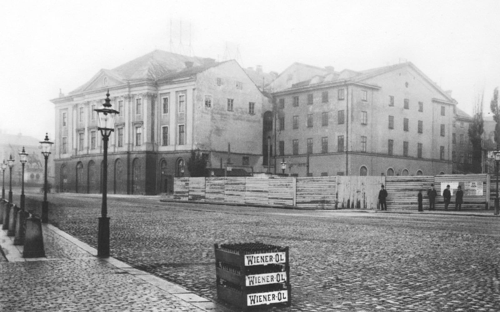 Ett stort gammalt stenhus vid ett kullerstenstorg, fotograferat kort innan det revs
