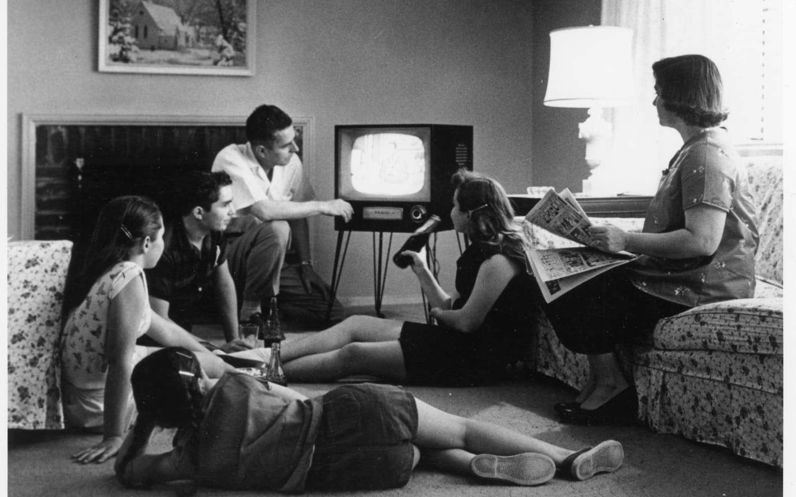 Svartvitt foto av en familj i ett vardagsrum som tittar på en tv, några sitter på golvet