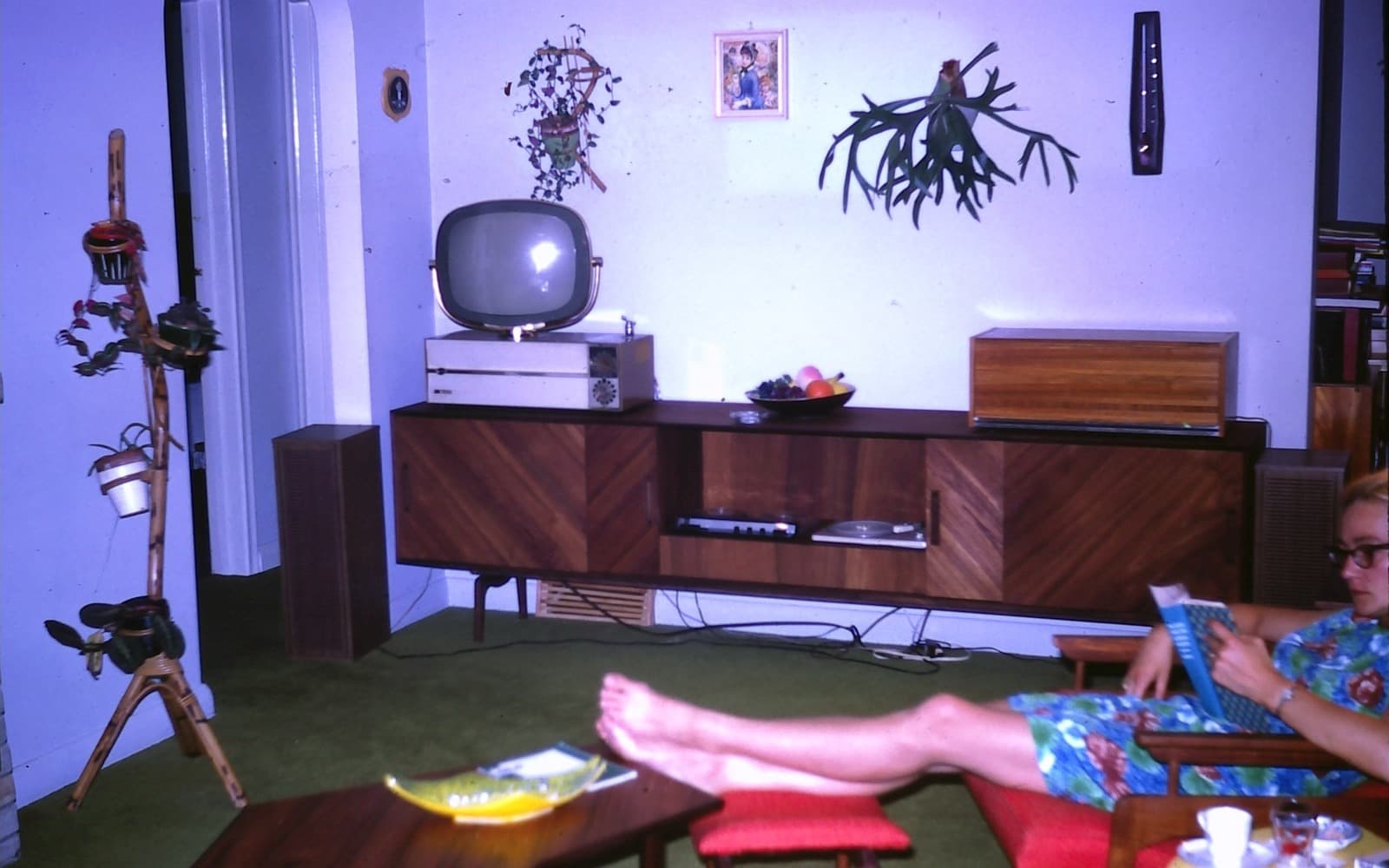 Ett färgglatt vardagsrum från 1960-talet med en tv på en sideboard och en kvinna som läser i en fåtölj