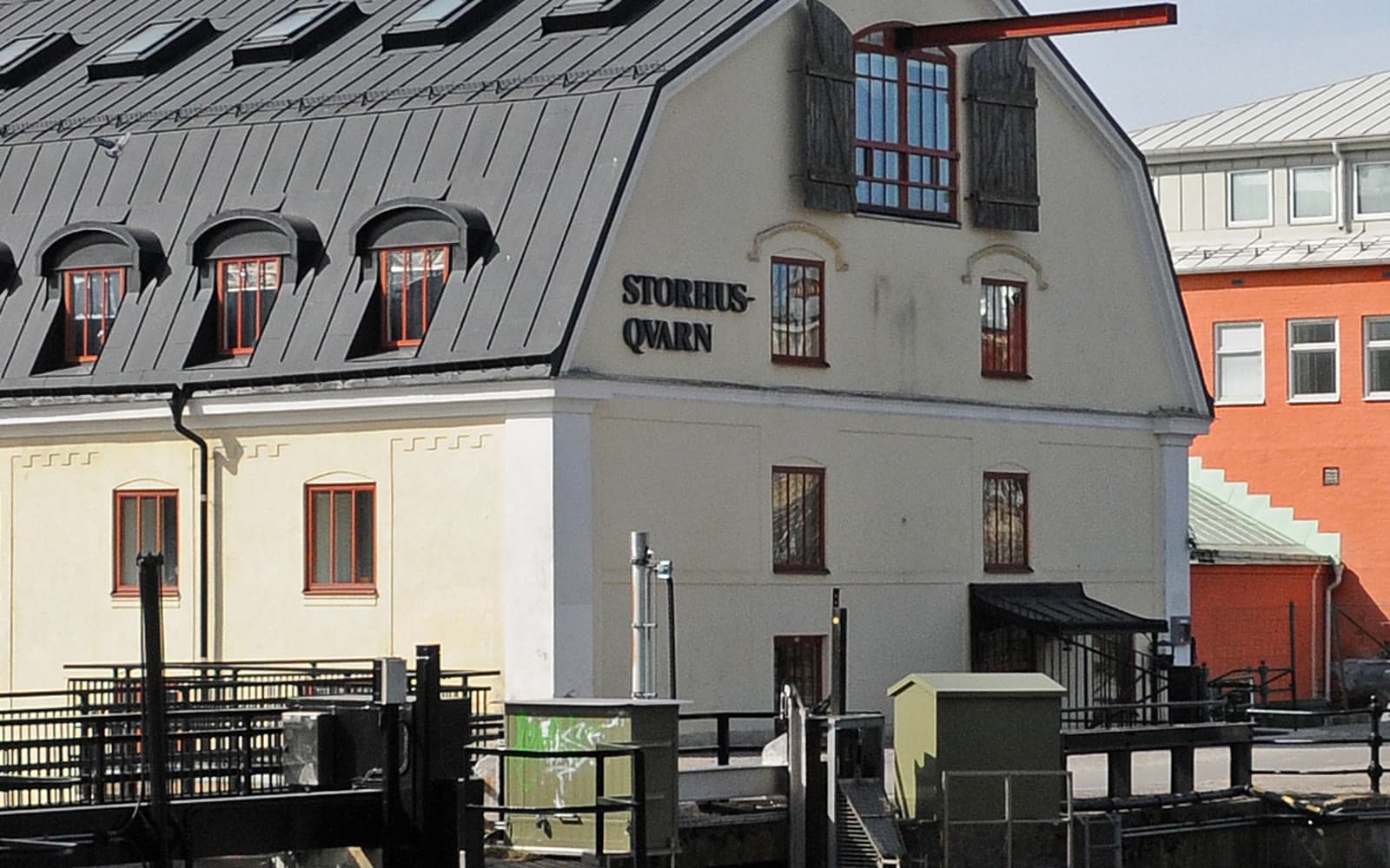 Ljus kvarnbyggnad med mörkgrått tak och texten STORHUS-QVARN på gaveln, vid en å.