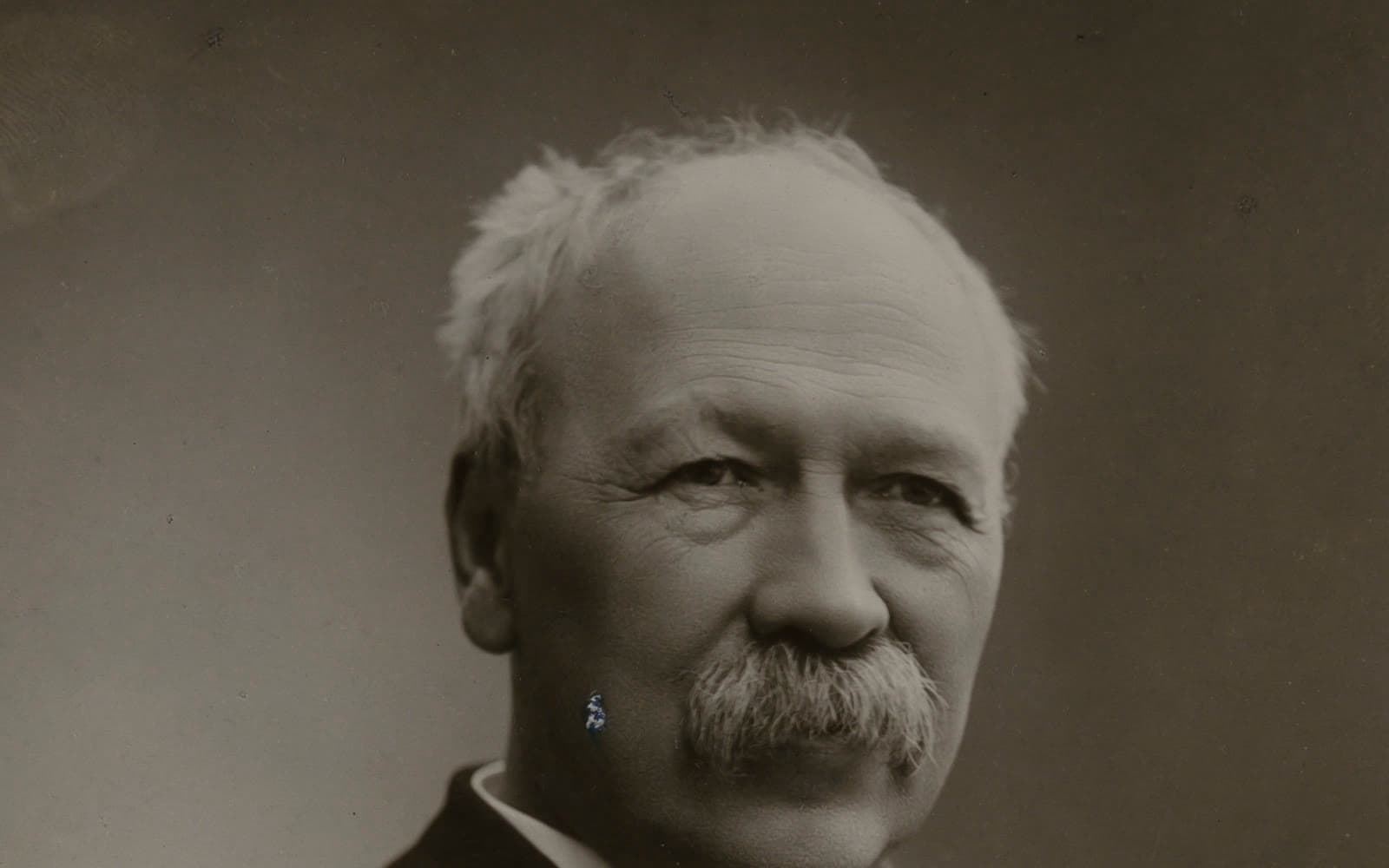 Svartvitt porträtt av en äldre man med vitt hår och stor gråvit mustasch.