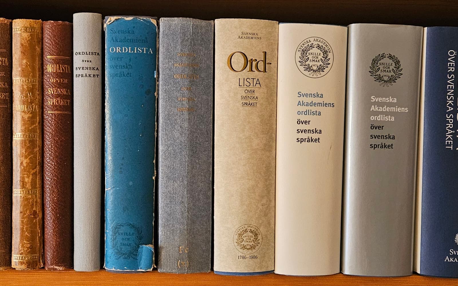 En hylla med Svenska Akademiens ordlista i många olika upplagor, från gamla bruna band till nya.