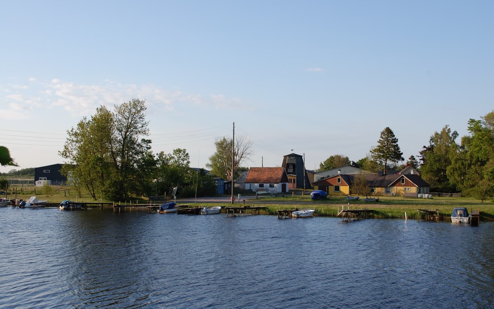 Ett lugnt vattendrag en sommarkväll med små båtar, bryggor och hus vid stranden