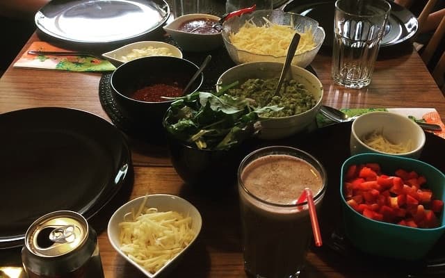 Ett dukat bord med skålar med riven ost, tomater, guacamole och salsa till tacos