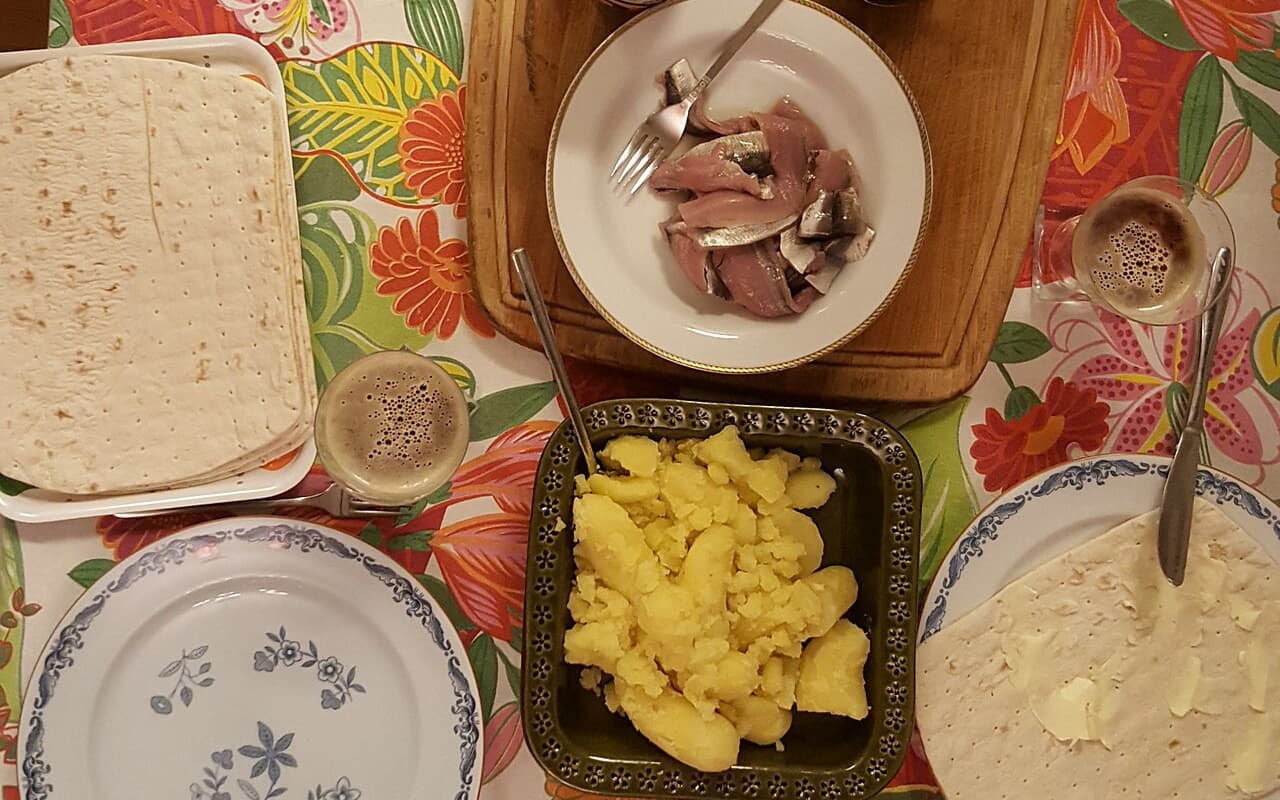 Ett dukat bord med tunnbröd, potatis, rödlök och en tallrik surströmming