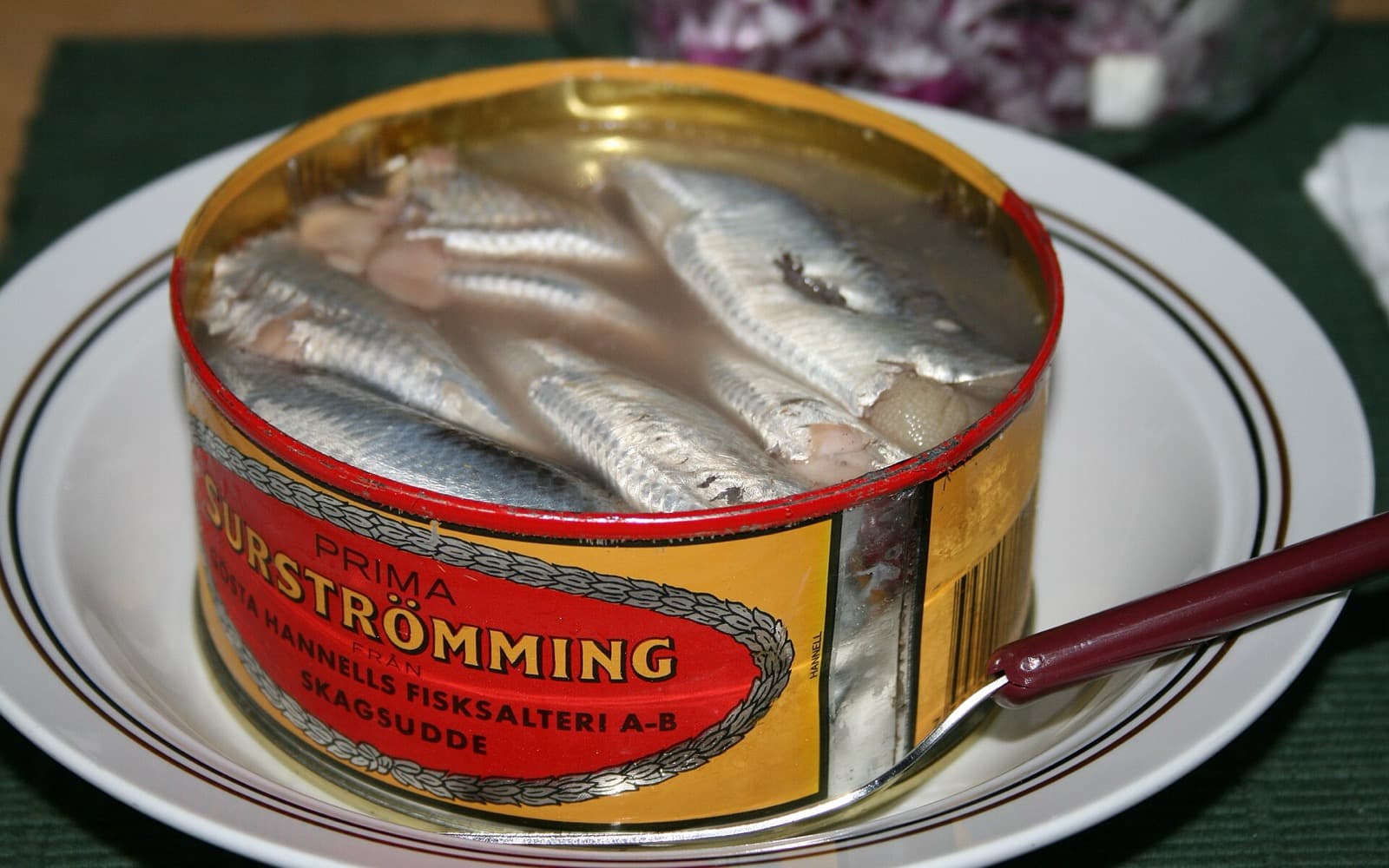 En öppnad burk surströmming på en tallrik, med fiskarna synliga i lagen