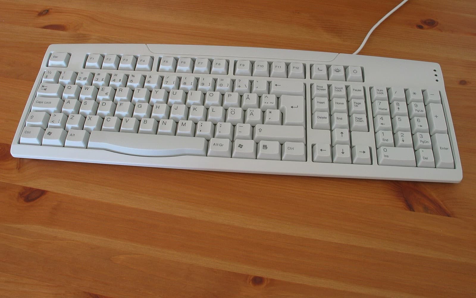 Ett ljusgrått tangentbord med svenska tangenter på ett träbord