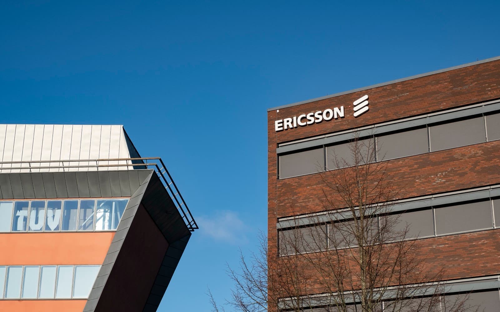 Två moderna kontorshus mot en klarblå himmel, det ena med Ericssons logga på fasaden