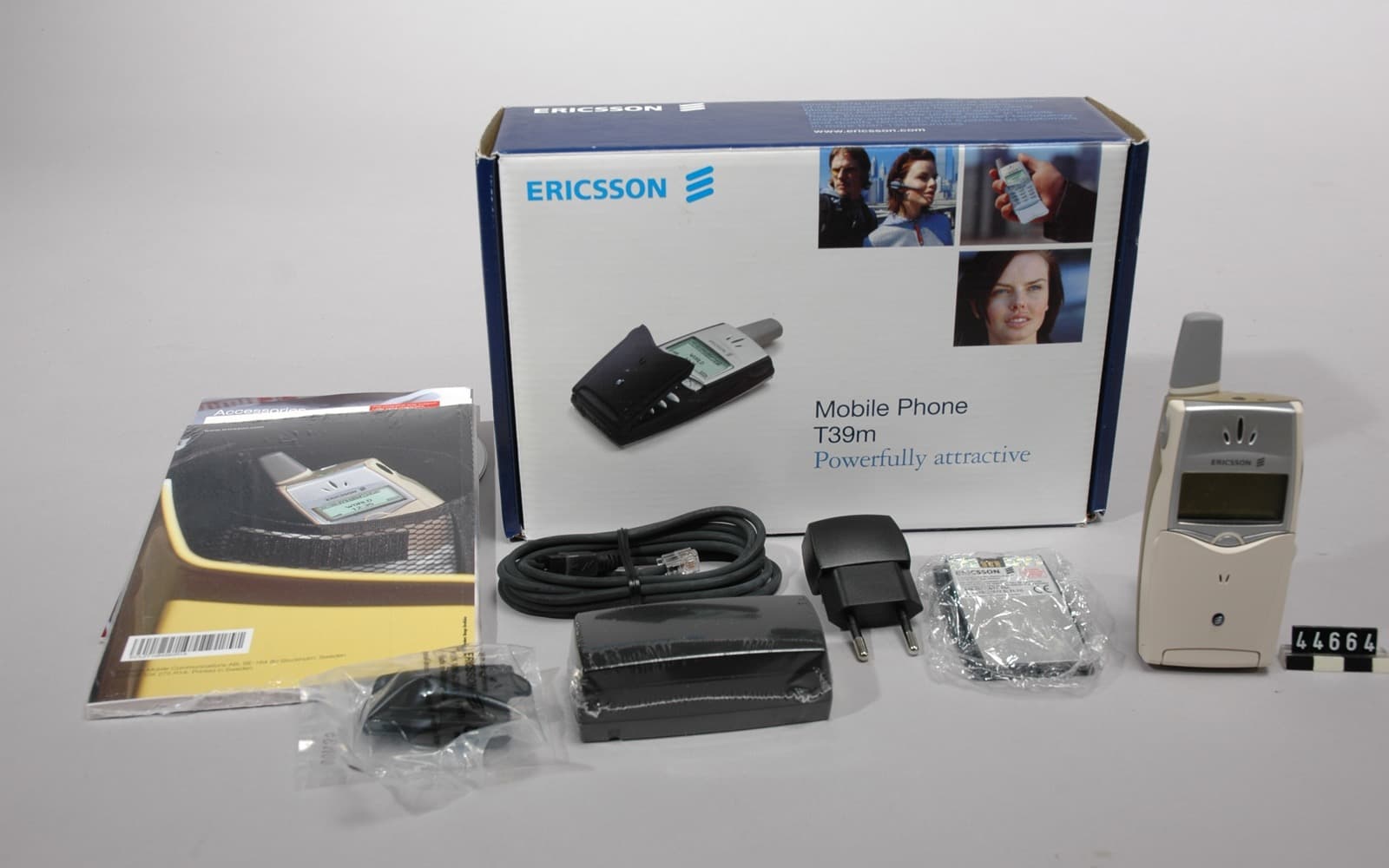 En silverfärgad mobiltelefon från Ericsson bredvid sin kartong, laddare, sladd och bruksanvisning