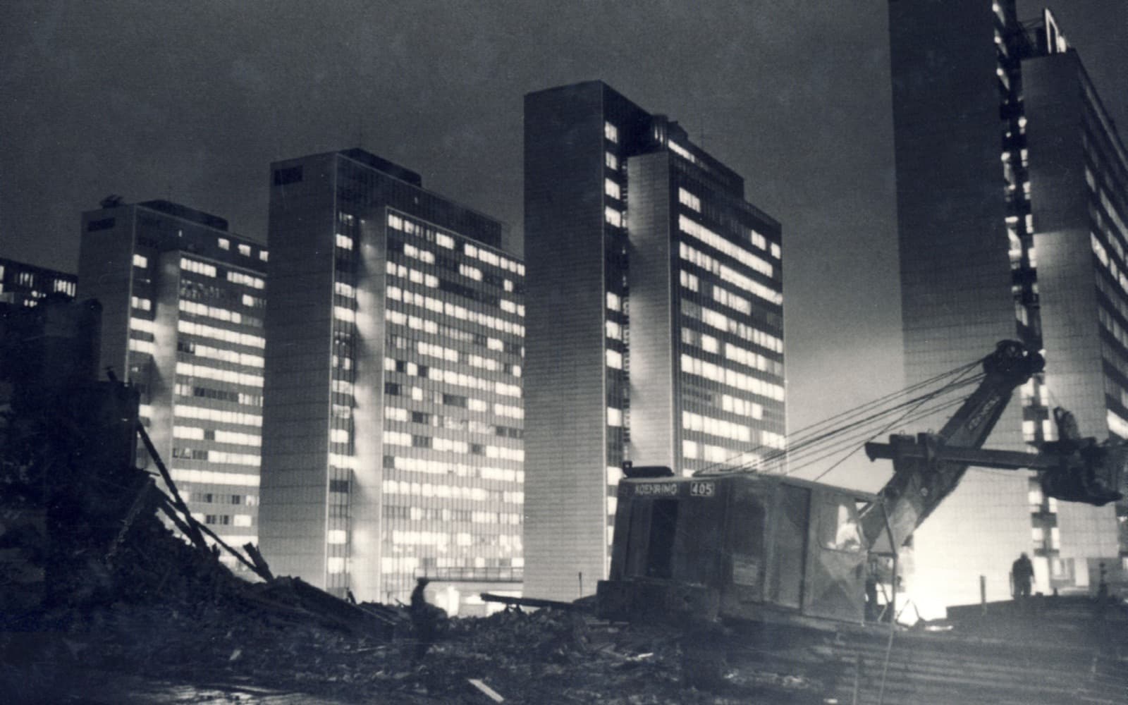 Svartvitt nattfoto av de nybyggda höghusen i Hötorgscity i Stockholm med upplysta kontorsfönster och rivningsmassor i förgrunden, 1962.