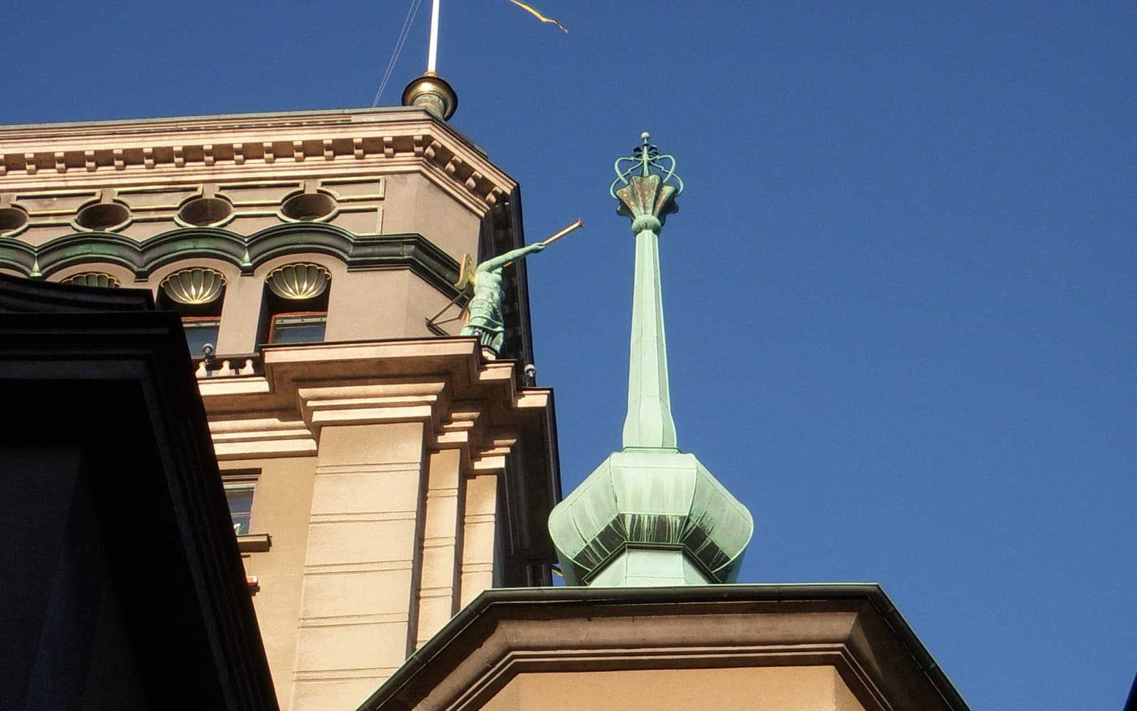 Toppen av ett gammalt stenhus med ett grönt kopparspira mot en klarblå himmel