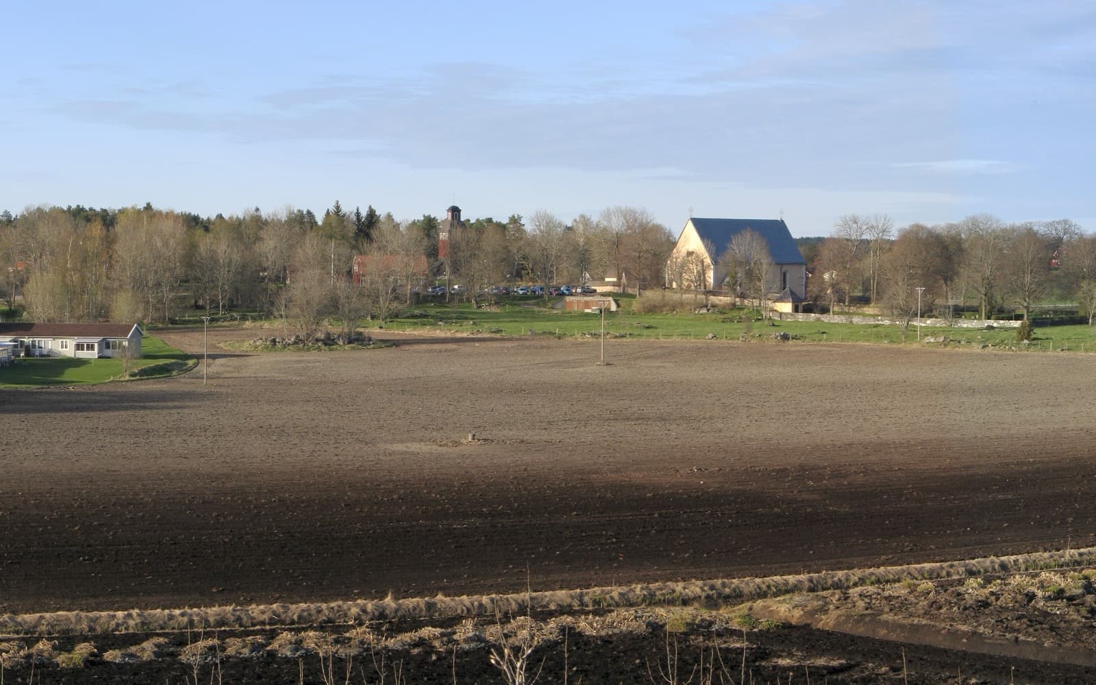 Vy över åkrar och byn Knutby i Uppland med träd och en vit kyrka i bakgrunden