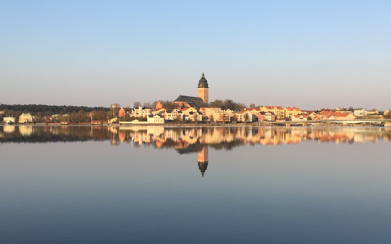 Strängnäs domkyrka och stadens hus speglar sig i ett blankt Mälaren en klar morgon.