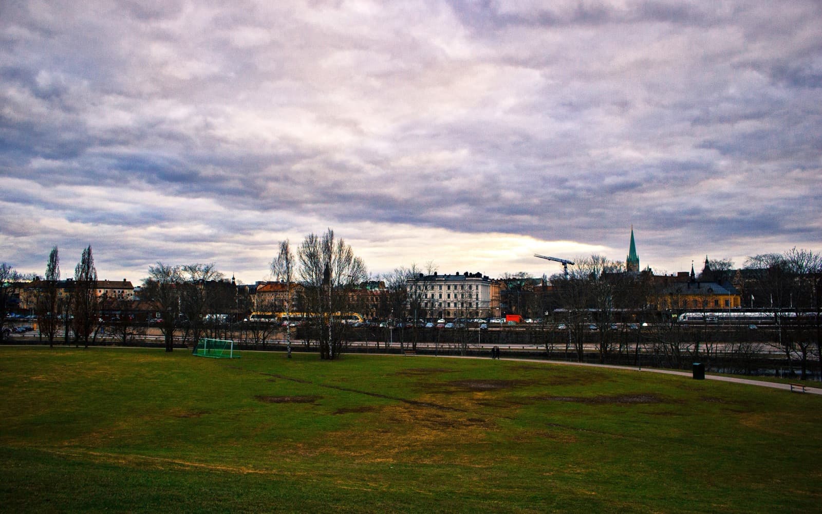 Utsikt över Linköping en molnig dag, med en gräsmatta i förgrunden och domkyrkans torn i bakgrunden