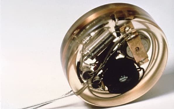 En rund, genomskinlig pacemaker med synliga elektroniska komponenter och en sladd