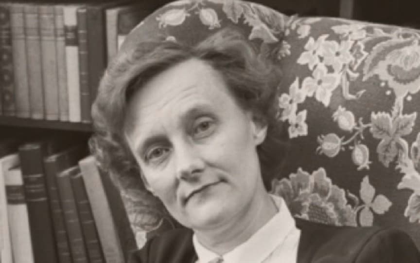 Porträtt av Astrid Lindgren i en blommig fåtölj framför en bokhylla