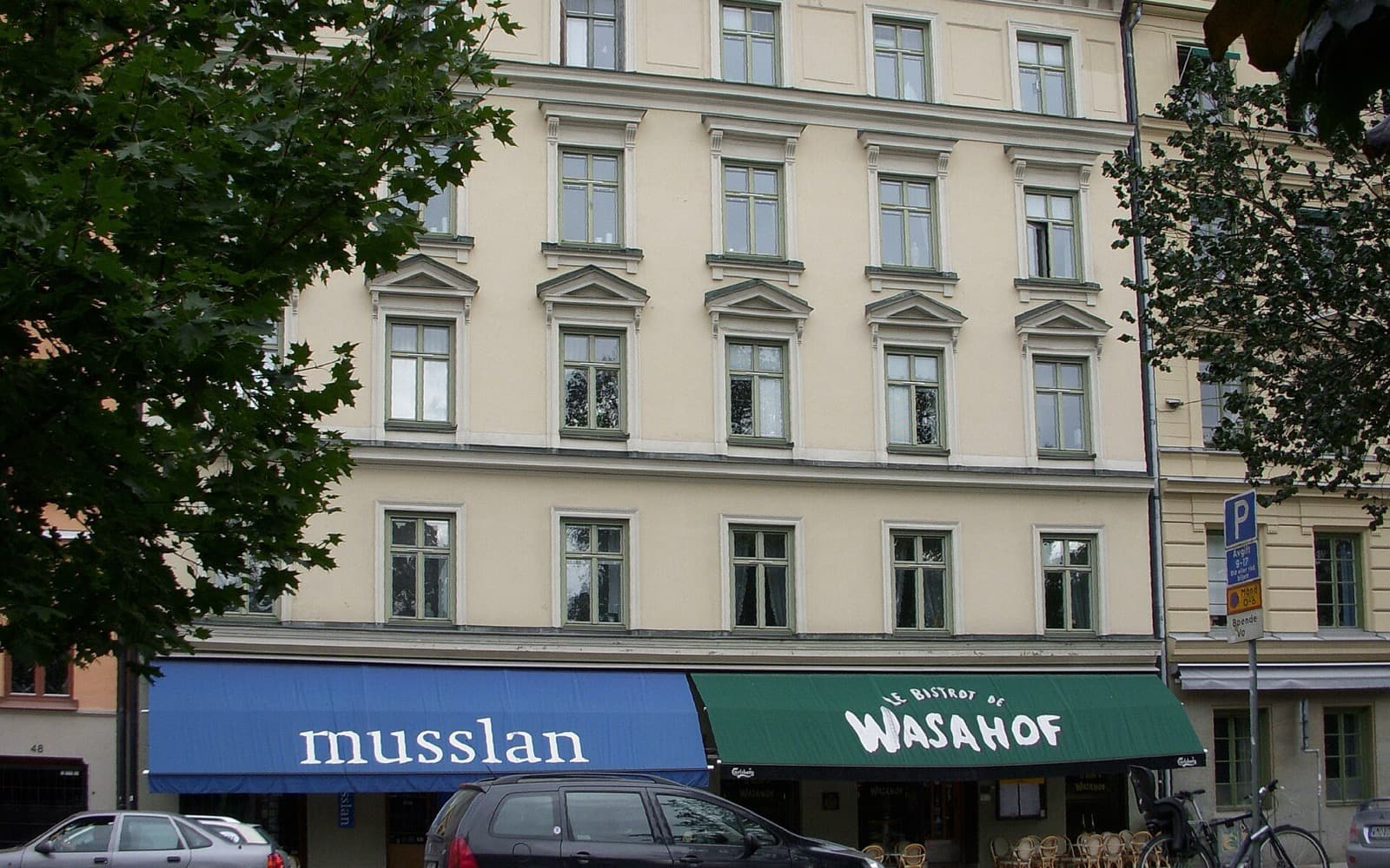 Fasaden på ett ljust flerbostadshus med markiser över två restauranger